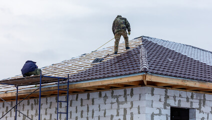 A man is working on a roof, and another man is standing on a ladder