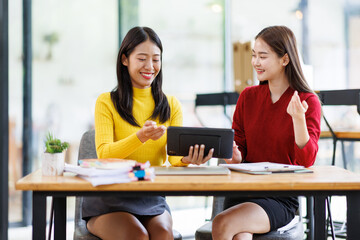 Obraz premium Shot of two businessasianwomen working together on digital tablet. Creative female executives meeting in an office using tablet pc and smiling. 