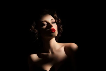 woman with red lipstick and a black background. The woman is looking at the camera. The image has a moody and dramatic feel to it © lashkhidzetim