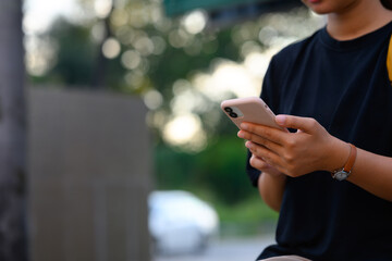 Close up of woman using smartphone while standing outdoors with a blurred natural background