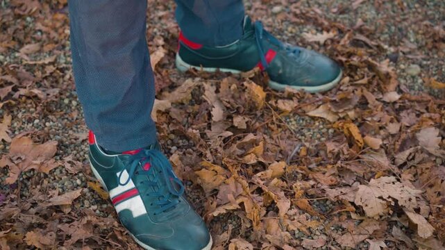 man in old schol Tisza brand blue, white and red sneakers standing on autumn brown and yellow fallen leaves close-up