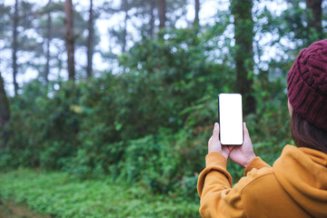 A woman holding mobile phone with blank white desktop screen in the forest