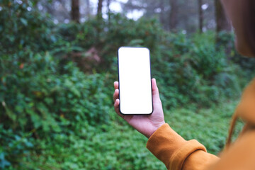 A woman holding mobile phone with blank white desktop screen in the forest