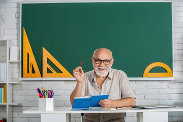 Portrait male teacher in classroom reads book. Old man teachers on green board. Male teacher with...