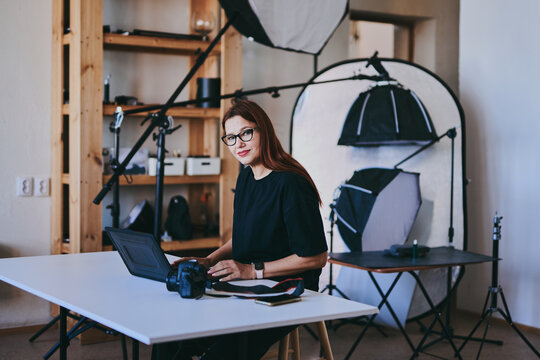 Female photographer with laptop on table processing shots in professional photo studio