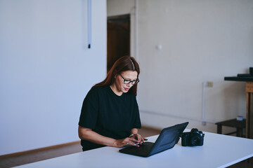 Female photographer with laptop on table processing shots in professional photo studio