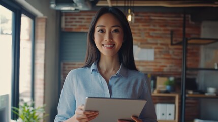 Happy young Asian saleswoman looking at camera welcoming client. Smiling woman executive manager, secretary offering professional business services holding digital tablet standing in office.