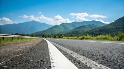 Fototapeta premium asphalt road with white lane divider leading to blurred green mountains and blue sky - road trip concept
