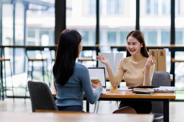 Two asian female creative agency casual meeting discussion working with laptop, analyze planning and financial statistics and investment market at office.
