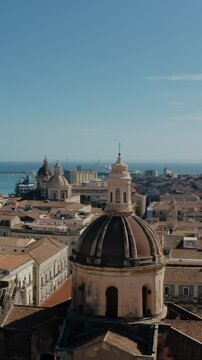 Vertical cinematic orbit drone flight around San Michele Arcangelo ai Minoriti Cathedral in Catania with sea port in the background. Catania old town from above. Architecture in Sicily.
