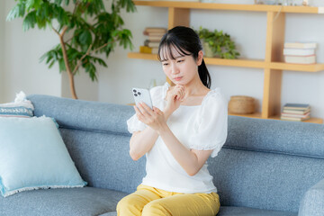 部屋でスマホを操作する若い女性