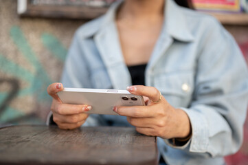 A close-up of a woman sits at an outdoor table of a cafe, using her smartphone, watching a video.