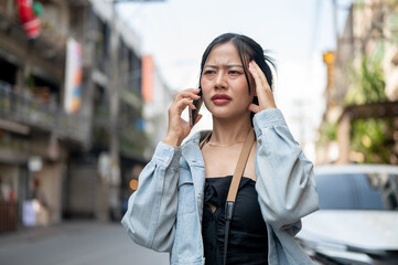 A confused female tourist talking on the phone with her taxi driver while walking down the street.