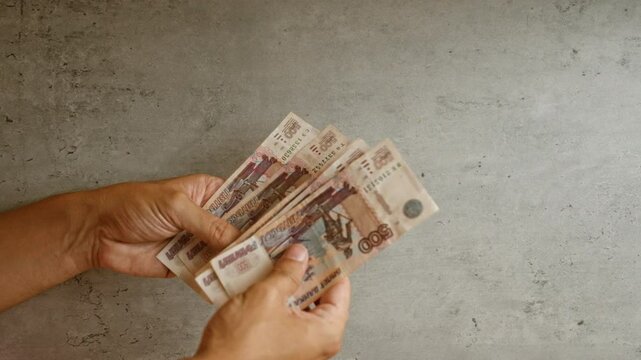 Hands counting multiple russian ruble banknotes against a concrete background