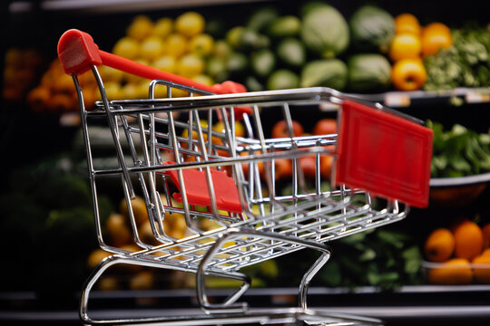 Bottom view of shopping cart with blurred supermarket fruit shelves in background, food shopping and sourcing concept