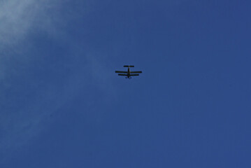 A small motor plane with two wings flies away into the distance in the middle of the blue sky.