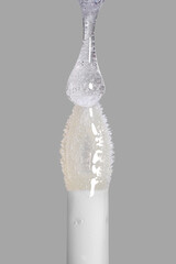 Drop of transparent liquid lip gloss falls on applicator. Closeup shot