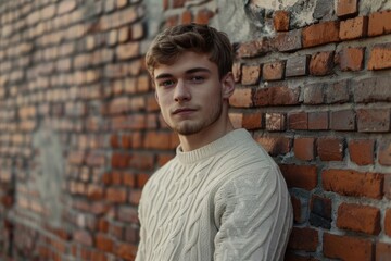 Obraz premium Attractive man in cozy sweater by brick wall.