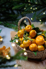 A woven basket filled with fresh mandarins surrounded by fir branches and warm fairy lights, creating a cozy festive atmosphere