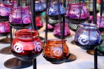 Triple decorative glass candlesticks. Colorful candle holders with metal legs and traditional patterns, hanging on chains. Home accessories. Lighting. Green, purple, red and blue candlesticks.
