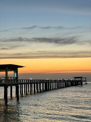 Fototapeta premium pier extending from the beach into the ocean toward orange sunrise.