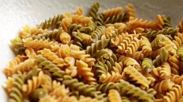 Raw spiral pasta closeup showcasing green and orange colors in a white ceramic bowl
