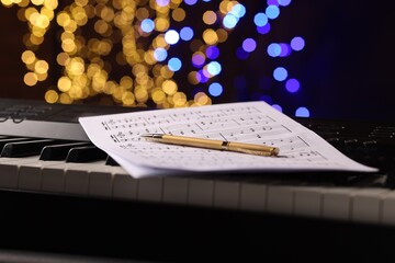 Sheets with notes and pen on piano against blurred lights, closeup. Bokeh effect