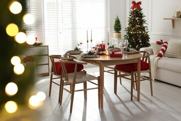 Christmas table setting with stylish dishware, glasses and burning candles in festive decorated room