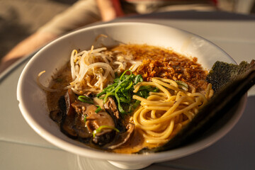 Vegan ramen closeup. Asian noodles with mushrooms, nori and greens, vegan dish in sunlight, street...