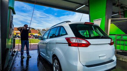A Caucasian man washing a white car at a self-service car wash, emphasizing cleanliness and vehicle...