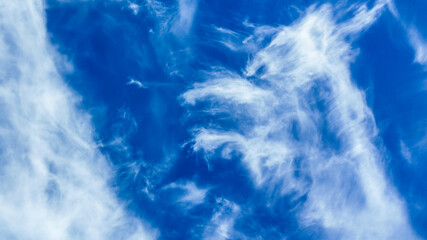 Wispy white clouds against a bright blue sky evoke peacefulness and relaxation, symbolizing freedom...