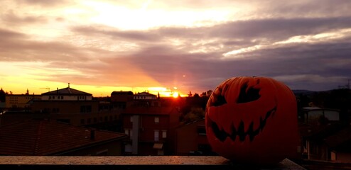 A beautifully carved pumpkin sits on a balcony, glowing softly at sunset