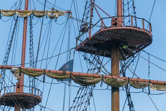 The masts, rigging, and crow's nest of a traditional sailing ship, highlighting intricate ropes, furled sails