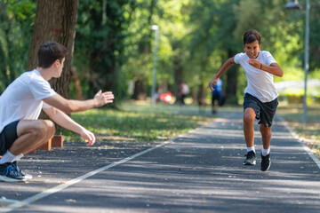 Fototapeta premium Trainer works with a boy to improve speed and running technique in the park. Focused on building agility and endurance, the outdoor training session promotes healthy physical activity for kids.