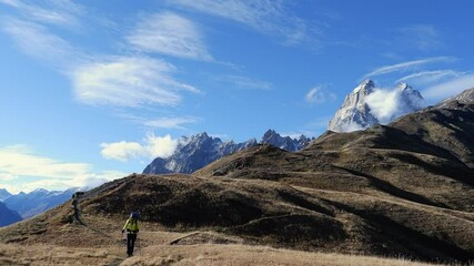 Female backpacker hikes on meadow trail below snowy alpine mountains - Powered by Adobe