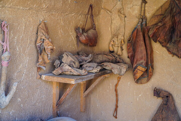 A rustic interior showing ancient tools and leather goods hanging on an adobe wall. A glimpse into a bygone era. Ancient Artisan's Workshop.