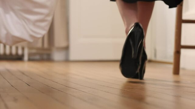 Woman walking away in black heels on a wooden floor, ground level shot