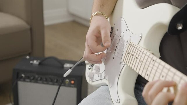 Strumming a white Stratocaster style electric guitar with a small amplifier in the background.