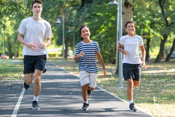 Sports trainer running with two boys during an outdoor exercise session. The activity focuses on building endurance, coordination, and teamwork in a fun, supportive environment.