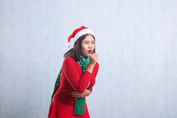 gesture of adult woman wearing christmas sweater, Santa hat and scarf, left slanted severe cough front view holding stomach, isolated on white background