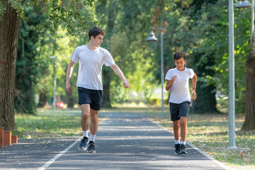 Fototapeta premium Trainer runs alongside two boys in a sunny park, focusing on improving their endurance and physical fitness. The boys are energized, learning proper running techniques while enjoying outdoor exercise