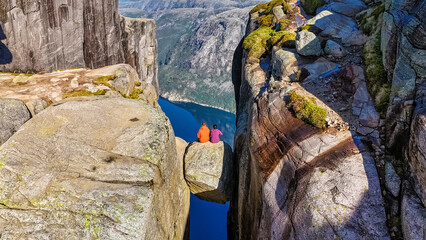 Two hikers sit on the edge of Kjeragbolten Pulpit Rock in Norway, enjoying the stunning panoramic view of the surrounding mountains and fjord © Fokke Baarssen