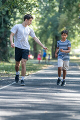 Fototapeta premium Trainer runs alongside two boys in a sunny park, focusing on improving their endurance and physical fitness. The boys are energized, learning proper running techniques while enjoying outdoor exercise