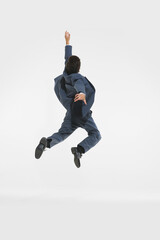Businessman in blue suit jumping with one arm raised, capturing ambition and enthusiasm in professional setting on white background. Full-length back view. Concept of business, achievement, success