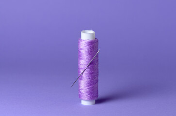 Purple violet thread spool with needle close-up flat lay top view background with copy space for text