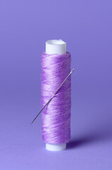 Purple violet thread spool with needle close-up flat lay top view background with copy space for...