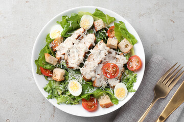 Tasty Caesar salad with chicken and tomatoes in bowl served on gray textured table, flat lay