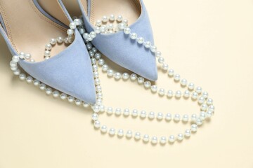 Stylish shoes and pearl necklace on beige background, closeup