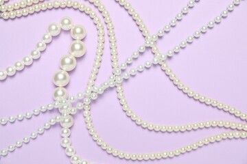 Beautiful pearl necklaces on violet background, flat lay