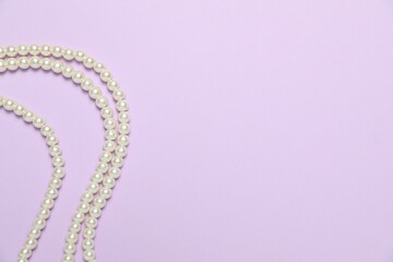 Beautiful pearl necklaces on violet background, flat lay. Space for text